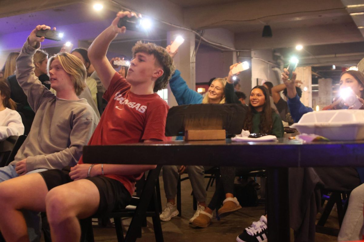 Students hold their phone flashlights in the air while they sing along to karaoke. 