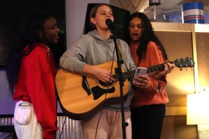 Strumming her guitar, junior Sienna Suderman sings along with juniors Esther Kisivo and Aleesha Fisher while they sing "Home" by Philips Phillips, Tuesday Dec. 10. 