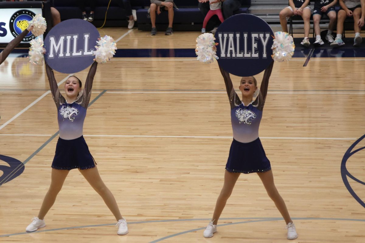 Freshman Stella Goodman and junior Bailey Bret hold up signs that together spell “Mill Valley” during the Silver Stars dance performance at the basketball scrimmage on Friday, Dec. 6. 