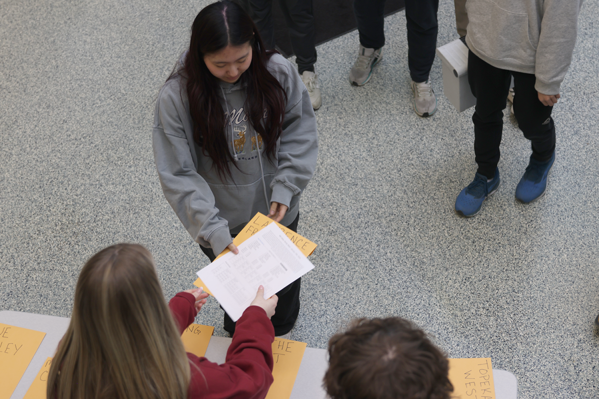 Junior Elaina Weese greets a team from Lawrence Free State High School at the main entrance.