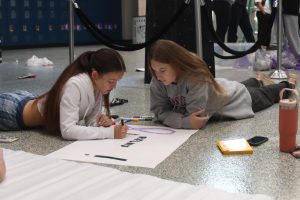 Seniors Stella Platt and Talia Delperdang use markers to create different Relay for Life posters to decorate lockers for Purple Bomb on January 20. 