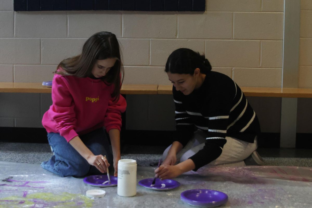 Sophomores Victoria Guess and Taleen Elkhatib paint on letters to spell "Relay for Life" on plates to hang them on the lockers during the setup of Purple Bomb on January 20. 