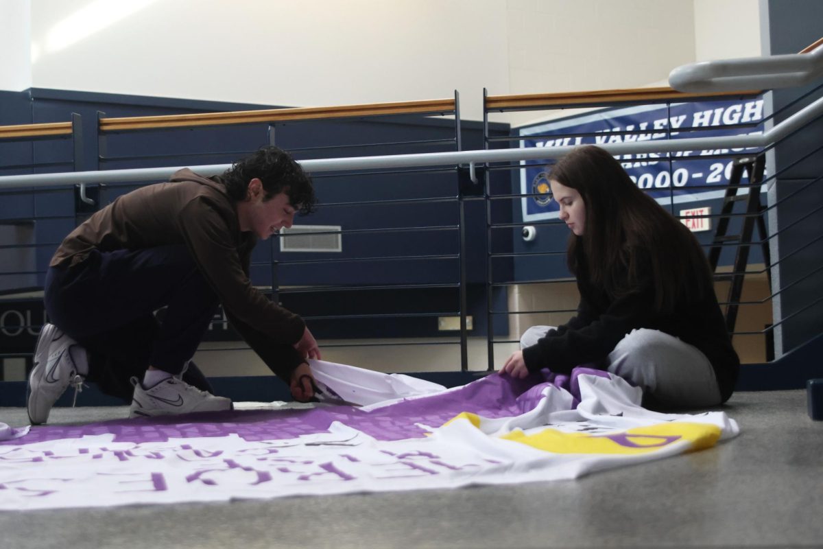 Seniors Maddox Walker and Emma Ronning cut the size of a Relay for Life poster to hang it behind the jaguar on the main staircase for Purple Bomb. 