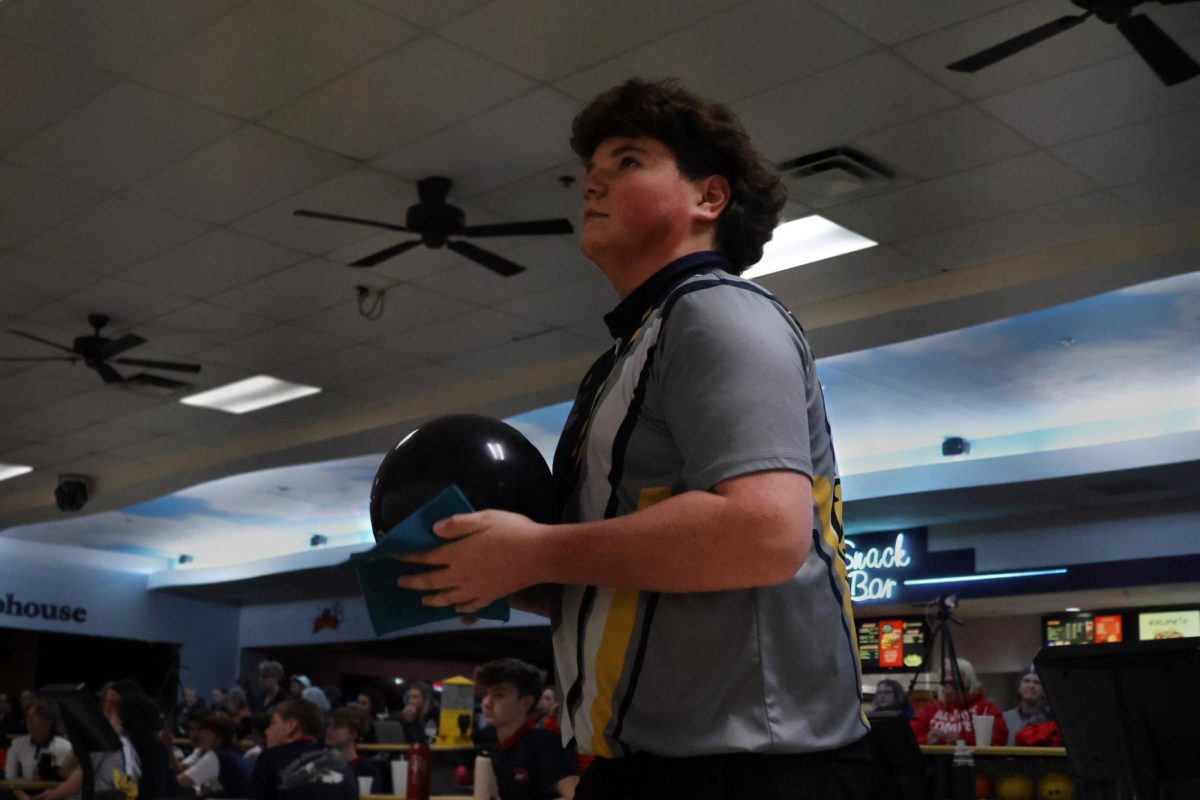 Wiping down his bowling ball before his turn, sophomore Ian Field looks up at the scoreboard.