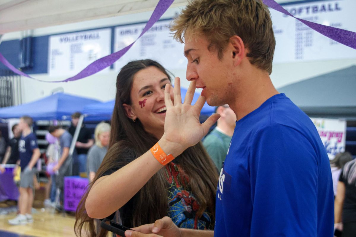 With a smile, junior Paige Roth paints senior Carter Clines face with glitter. 